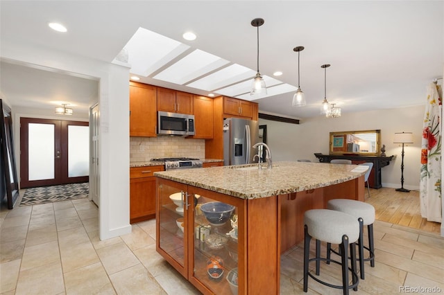 kitchen featuring light stone countertops, decorative light fixtures, stainless steel appliances, an island with sink, and tasteful backsplash