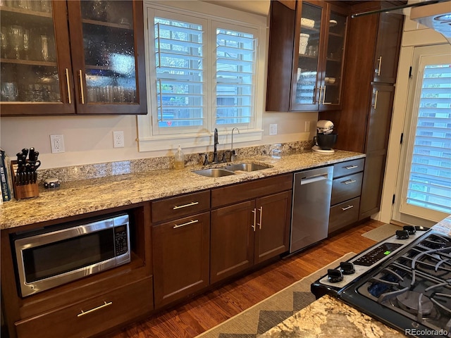 kitchen featuring glass insert cabinets, dark wood-type flooring, light stone counters, a sink, and stainless steel appliances