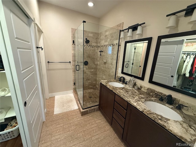 full bathroom with double vanity, a sink, a walk in closet, and a shower stall