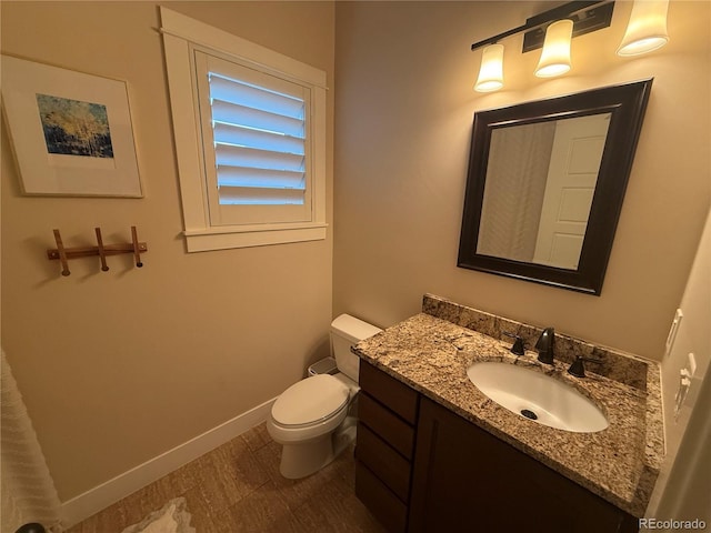 half bath with baseboards, vanity, and toilet