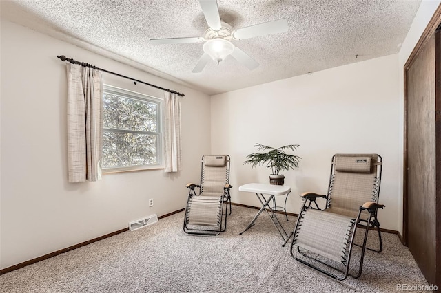 sitting room featuring ceiling fan, carpet, and a textured ceiling