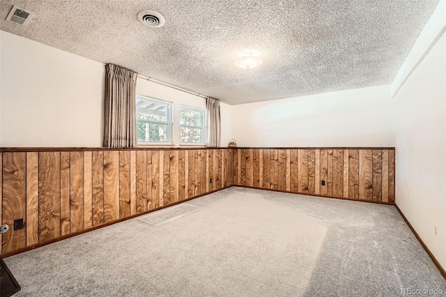 additional living space featuring wooden walls, light colored carpet, and a textured ceiling