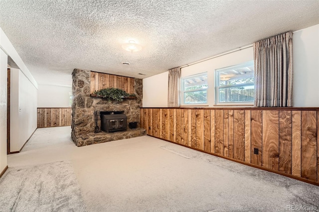 unfurnished living room with a wood stove, wooden walls, light carpet, and a textured ceiling