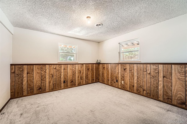 carpeted spare room featuring wood walls and a textured ceiling