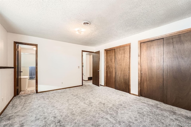 unfurnished bedroom with carpet, ensuite bathroom, a textured ceiling, and two closets