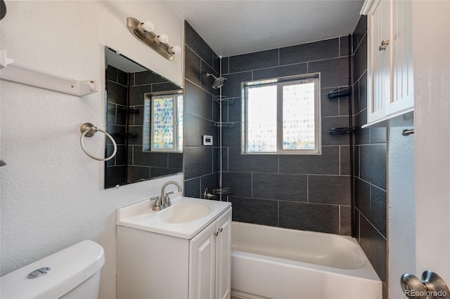 full bathroom featuring tiled shower / bath, vanity, and toilet