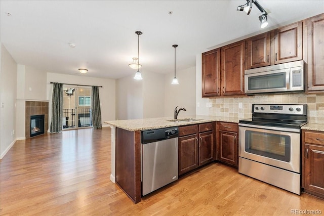 kitchen featuring sink, decorative light fixtures, kitchen peninsula, stainless steel appliances, and light hardwood / wood-style floors