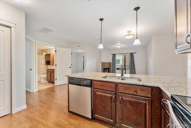 kitchen with appliances with stainless steel finishes, sink, hanging light fixtures, light stone countertops, and light wood-type flooring