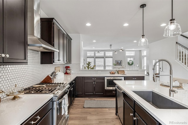 11027 Sunshimmer Cir, Parker, CO 80134 - kitchen with wall chimney range hood, stainless steel appliances, a sink, dark brown cabinets, and recessed lighting