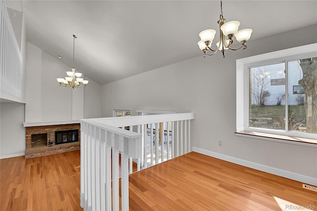 hall featuring baseboards, wood finished floors, a chandelier, and vaulted ceiling