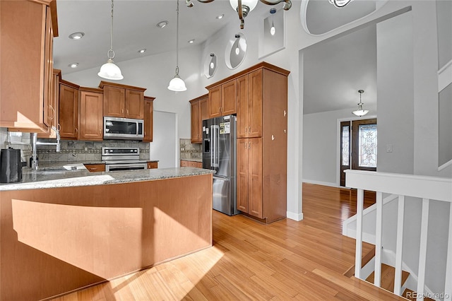 kitchen featuring light stone counters, a peninsula, light wood-style floors, stainless steel appliances, and a sink