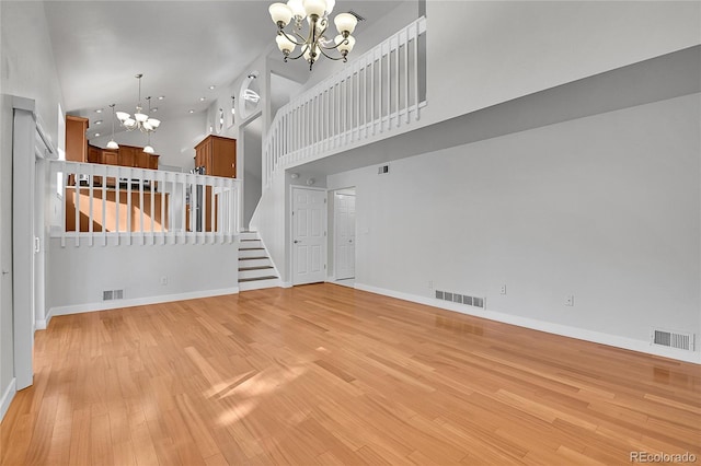 unfurnished living room with visible vents, light wood-style floors, a high ceiling, and a chandelier