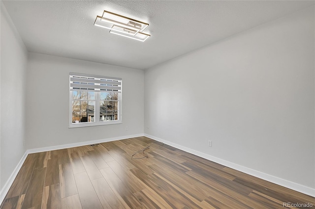 unfurnished room featuring visible vents, baseboards, a textured ceiling, and dark wood-style floors