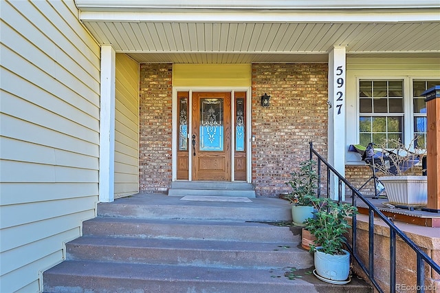 entrance to property with a porch and brick siding