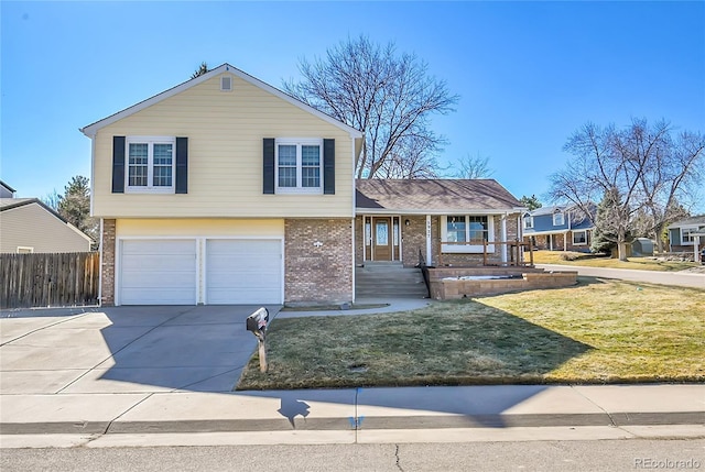 tri-level home featuring a front lawn, driveway, a porch, fence, and brick siding