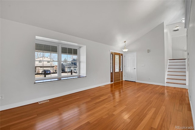 empty room with visible vents, baseboards, stairs, vaulted ceiling, and light wood-style floors