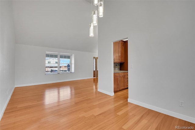 unfurnished living room with light wood-type flooring, baseboards, and a towering ceiling