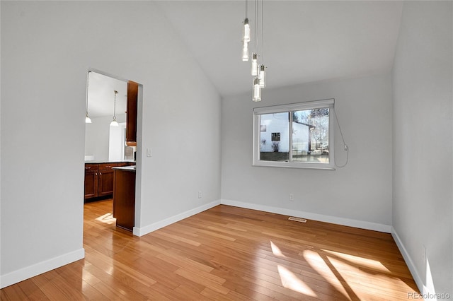 unfurnished dining area featuring visible vents, baseboards, lofted ceiling, and light wood-style floors