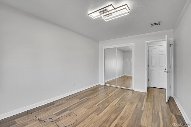 unfurnished bedroom with visible vents, baseboards, a closet, and wood finished floors