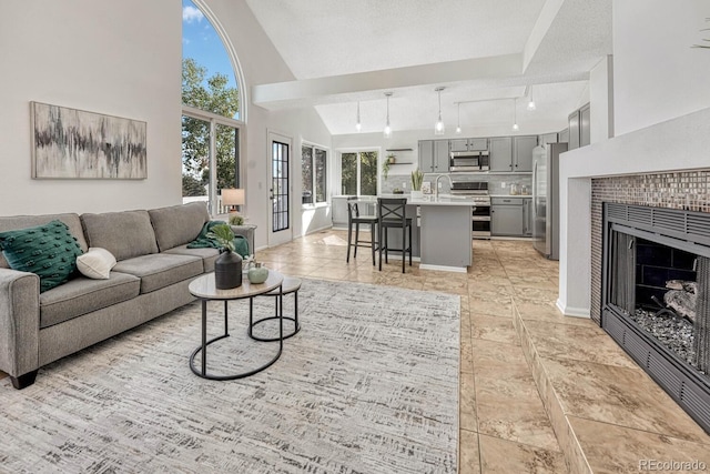 living area with a wealth of natural light, a tile fireplace, high vaulted ceiling, and baseboards