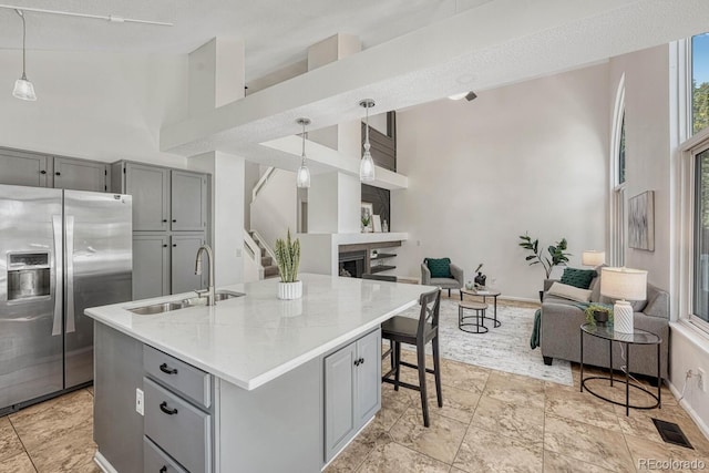 kitchen with high vaulted ceiling, a sink, gray cabinetry, stainless steel refrigerator with ice dispenser, and open floor plan