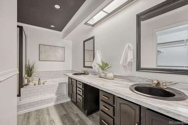 bathroom with double vanity, a bath, wood finished floors, and a sink