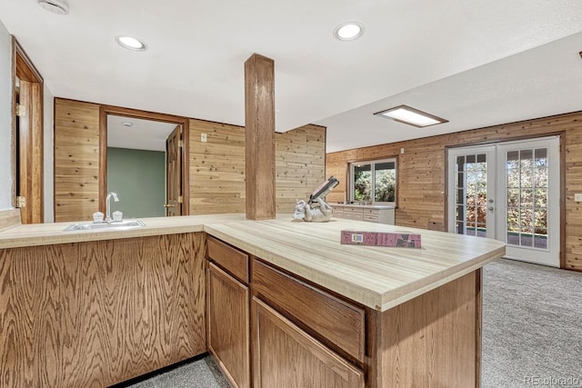 kitchen featuring light carpet, a sink, french doors, wooden walls, and light countertops