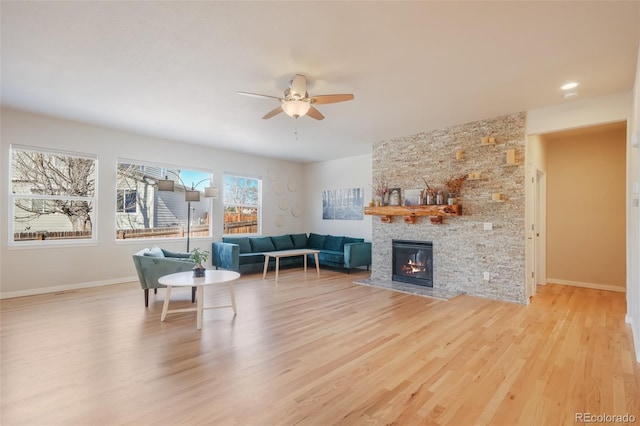 living room featuring ceiling fan, a large fireplace, and light hardwood / wood-style flooring