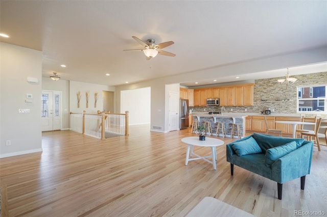 living room with light hardwood / wood-style floors and ceiling fan with notable chandelier