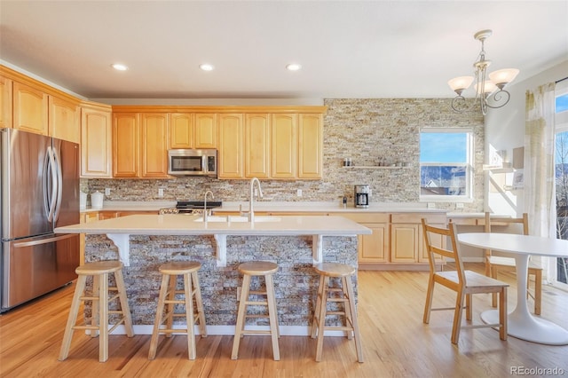 kitchen featuring tasteful backsplash, appliances with stainless steel finishes, a kitchen island with sink, and an inviting chandelier