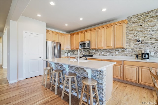 kitchen featuring appliances with stainless steel finishes, backsplash, light wood-type flooring, a breakfast bar, and a center island with sink