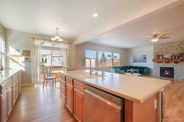 kitchen featuring an island with sink, ceiling fan with notable chandelier, a fireplace, stainless steel dishwasher, and sink