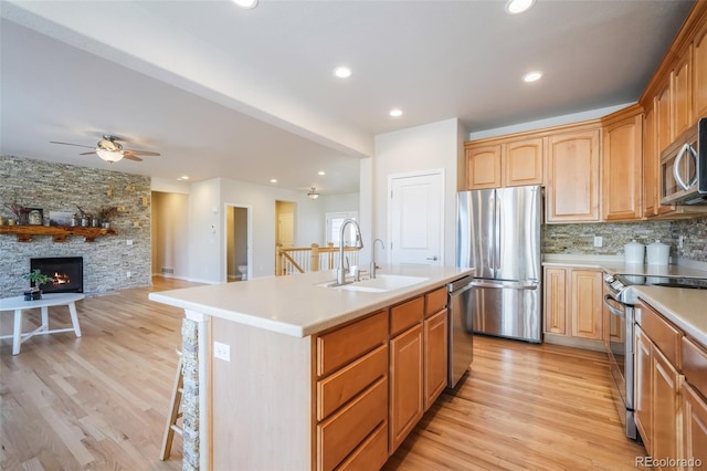 kitchen with decorative backsplash, sink, a kitchen island with sink, appliances with stainless steel finishes, and a stone fireplace