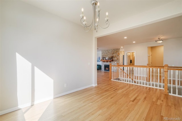 spare room with a fireplace, an inviting chandelier, and light hardwood / wood-style floors