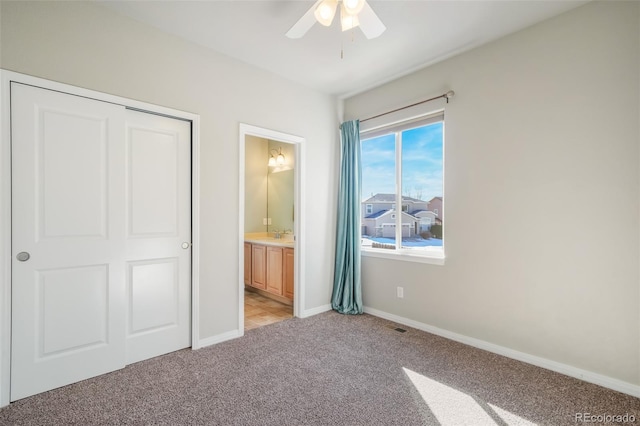 unfurnished bedroom with ceiling fan, ensuite bath, a closet, and light carpet