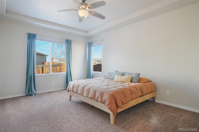 carpeted bedroom featuring ceiling fan and a raised ceiling