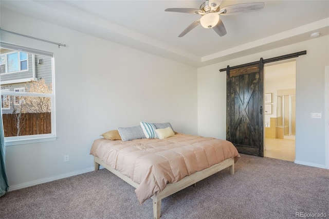 bedroom with a barn door, ceiling fan, a raised ceiling, carpet floors, and ensuite bath