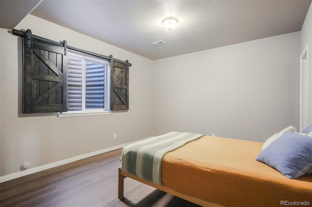 bedroom with a barn door and wood-type flooring