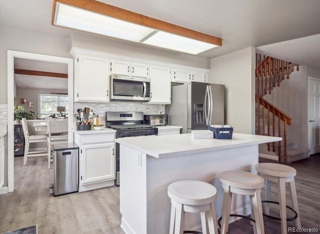 kitchen featuring a breakfast bar area, stainless steel appliances, white cabinetry, and light wood finished floors