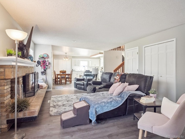 living room featuring a textured ceiling, a fireplace, wood finished floors, a notable chandelier, and stairs