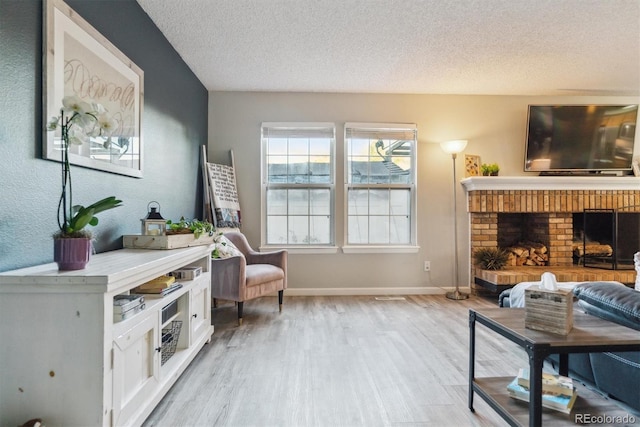 living area with a textured ceiling, baseboards, light wood finished floors, and a fireplace