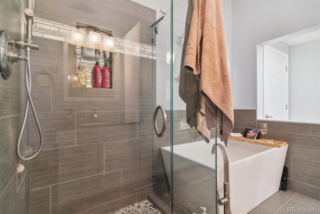 full bath with wainscoting, a shower stall, a soaking tub, and tile walls