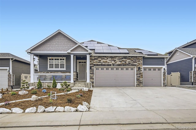 craftsman-style home featuring a porch, a garage, concrete driveway, roof mounted solar panels, and stone siding