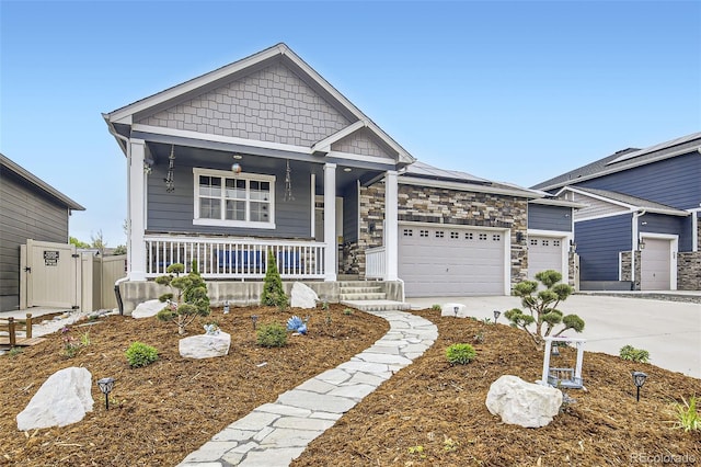 craftsman-style home with covered porch, driveway, a garage, solar panels, and stone siding
