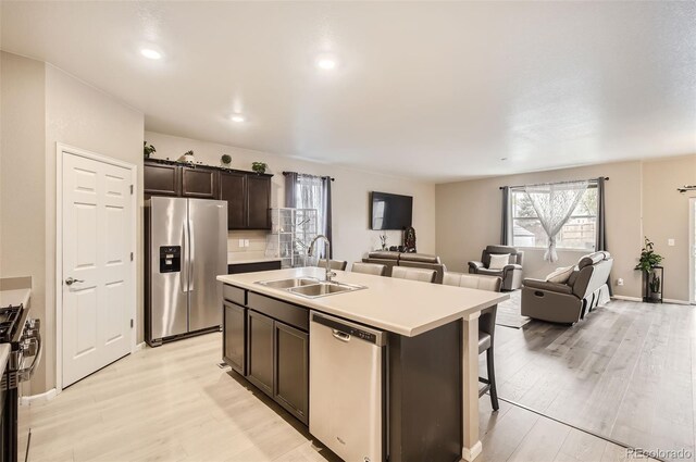 kitchen featuring appliances with stainless steel finishes, a sink, light wood-type flooring, a kitchen island with sink, and dark brown cabinets
