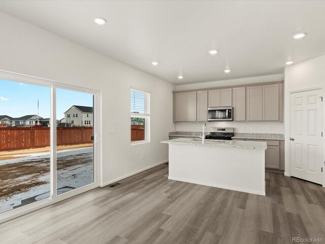 kitchen featuring a center island with sink, wood finished floors, gray cabinets, and appliances with stainless steel finishes