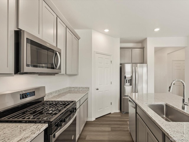 kitchen featuring light stone countertops, dark wood-style flooring, gray cabinetry, a sink, and appliances with stainless steel finishes