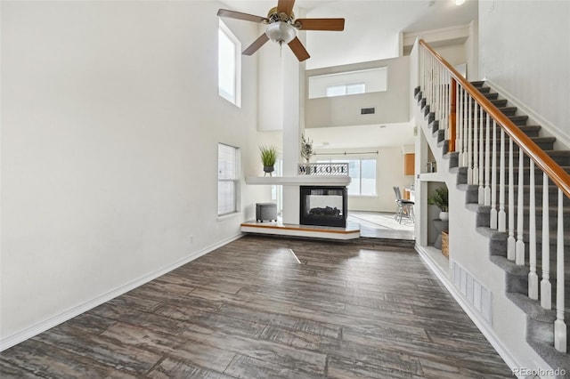 unfurnished living room with baseboards, a multi sided fireplace, stairs, wood finished floors, and a ceiling fan