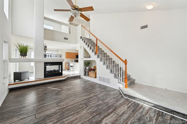 unfurnished living room with a multi sided fireplace, visible vents, stairs, and a ceiling fan