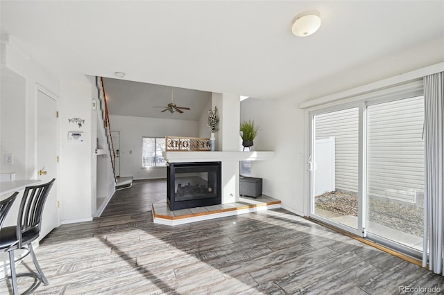 living room featuring wood finished floors, baseboards, lofted ceiling, a multi sided fireplace, and ceiling fan